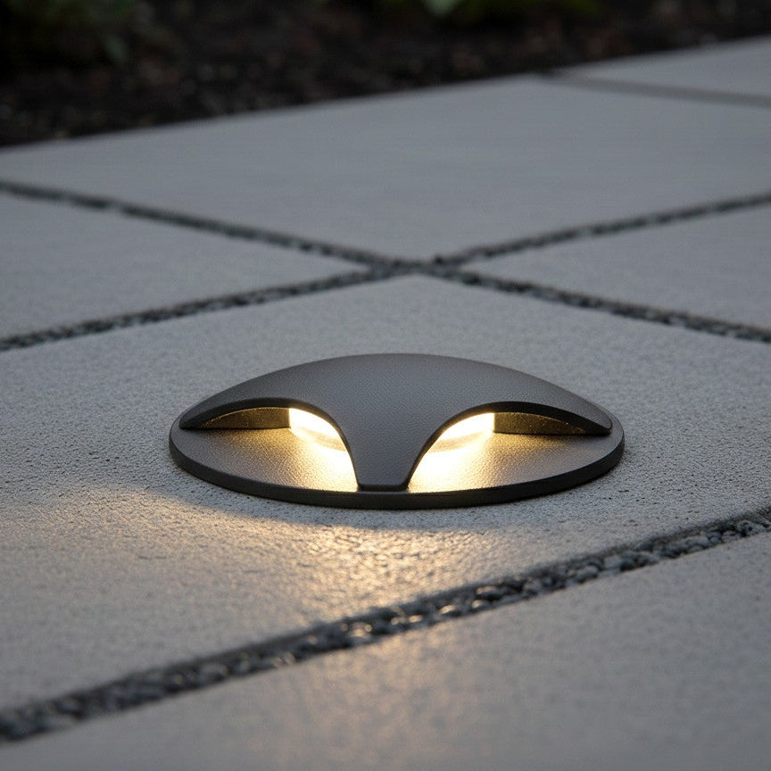 Dark grey ground light with two warm white lights on a grey paved surface
