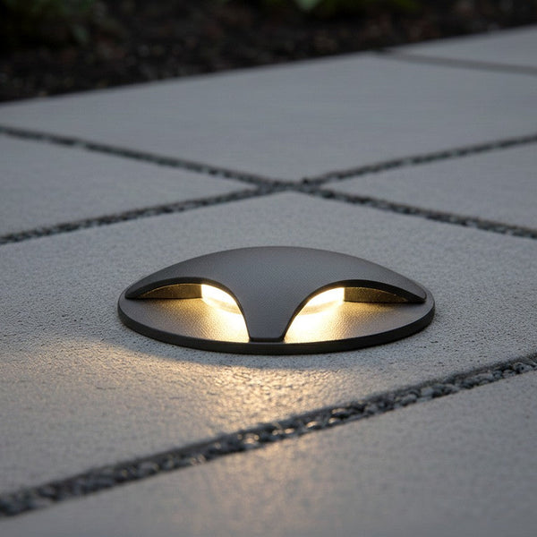Dark grey ground light with two warm white lights on a grey paved surface