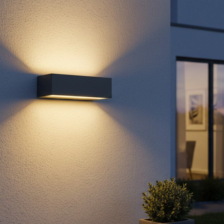 Rectangular outdoor wall light in dark grey casting light upwards and downwards on a textured wall