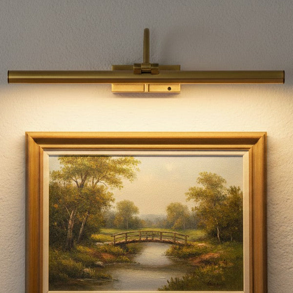 Brass picture light illuminating a framed landscape painting of a bridge over a river
