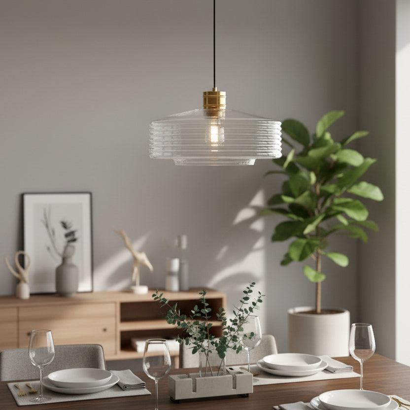 Clear glass pendant light with gold accents hanging over a dining table set with white plates and wine glasses