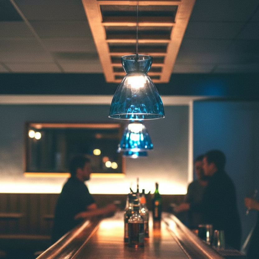 Blue glass pendant lights hanging above a wooden bar with bottles and people in the background