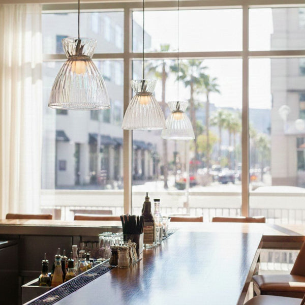 Three glass pendant lights hang above a bar with a large window overlooking a city street