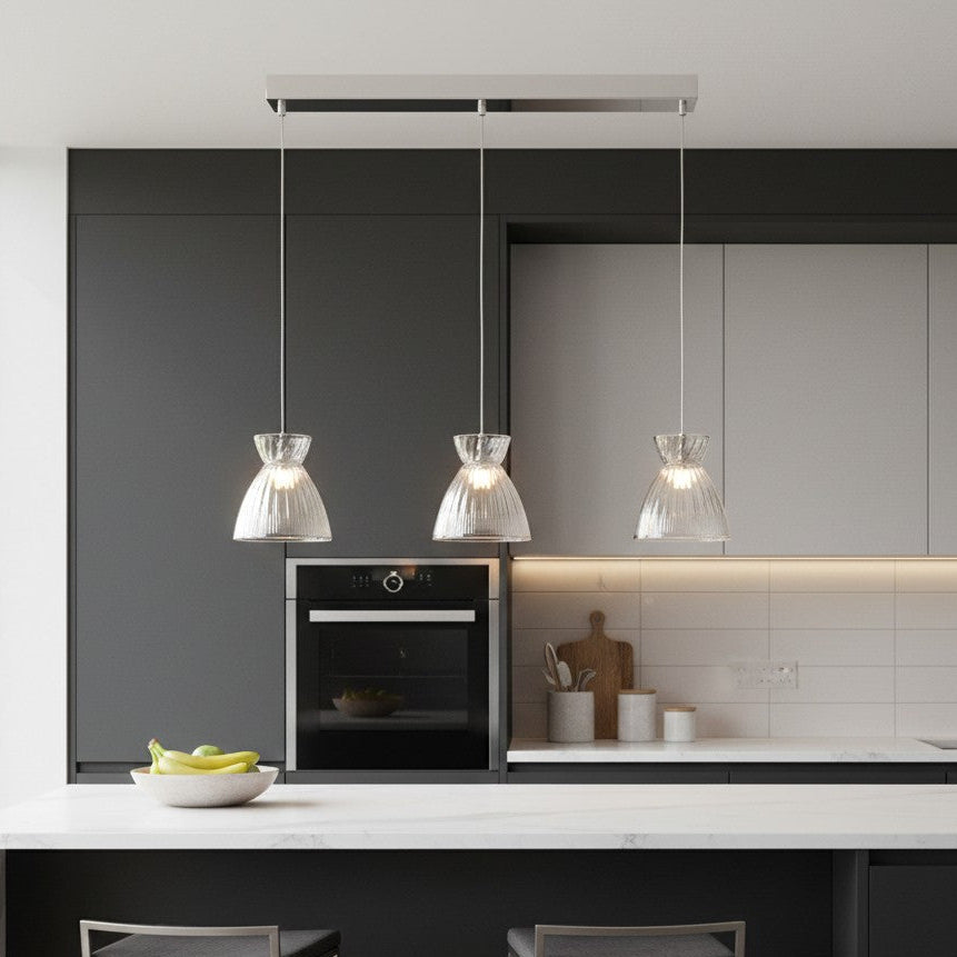 Three clear glass pendant lights hanging above a kitchen island with a bowl of fruit