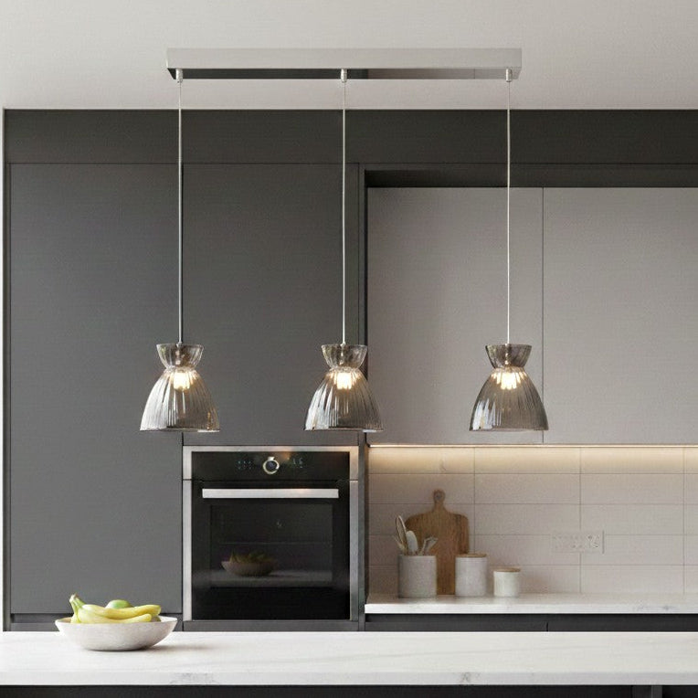 Three pendant lights with ribbed glass shades hanging over a kitchen island