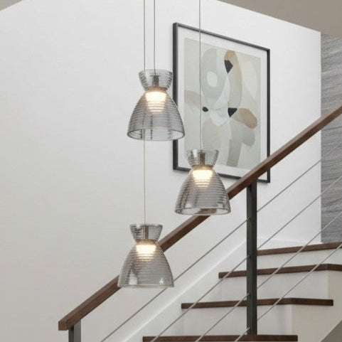 Three glass pendant lights hang at different heights above a wooden staircase with a black metal railing