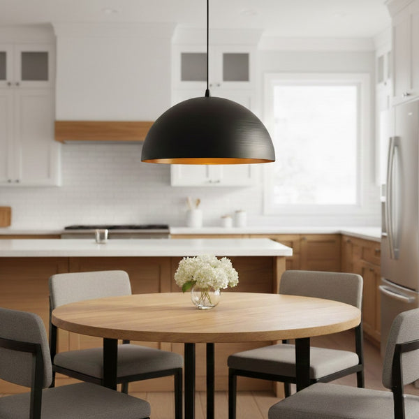 Black dome pendant light with a gold interior hanging over a round wooden dining table with four chairs