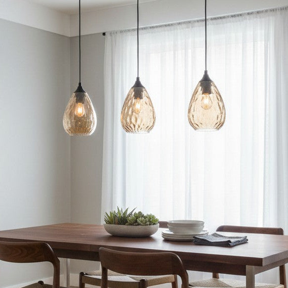 Three amber glass pendant lights hang above a wooden dining table with chairs and a succulent centerpiece