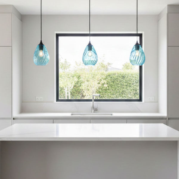 Three blue glass pendant lights hanging above a kitchen island with a sink and a window