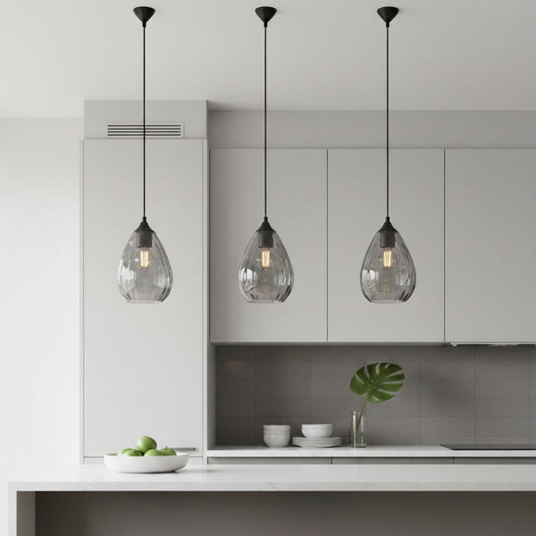 Three grey glass pendant lights with black fixtures hanging over a white kitchen island