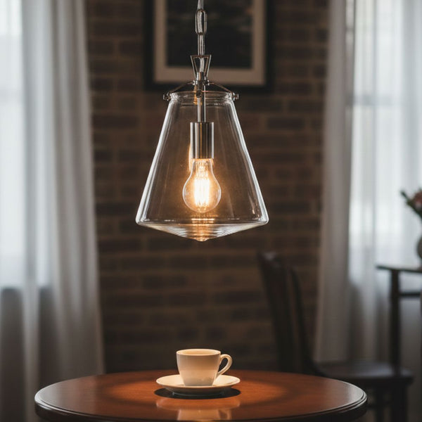 Glass pendant light with an exposed bulb hanging above a white coffee cup on a wooden table