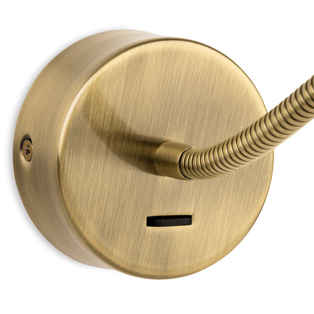 Close-up of a brass wall-mounted light fixture with a flexible arm and a rectangular switch