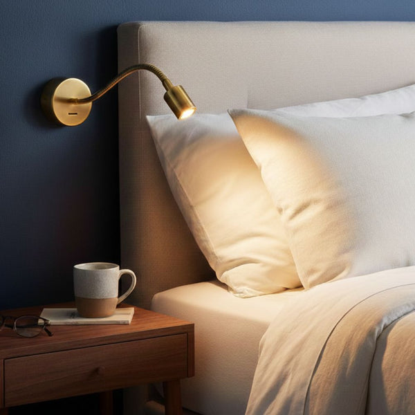 A brass wall-mounted reading light illuminates a bed with white pillows and duvet, next to a wooden nightstand