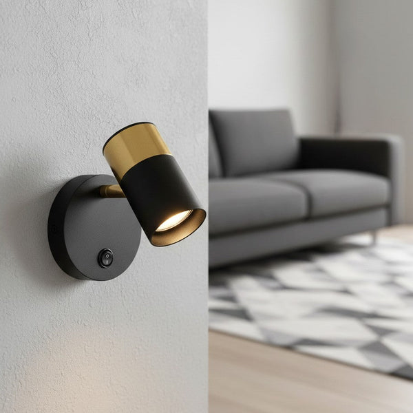 Black and gold wall-mounted spotlight with a switch, illuminating a white wall in a living room