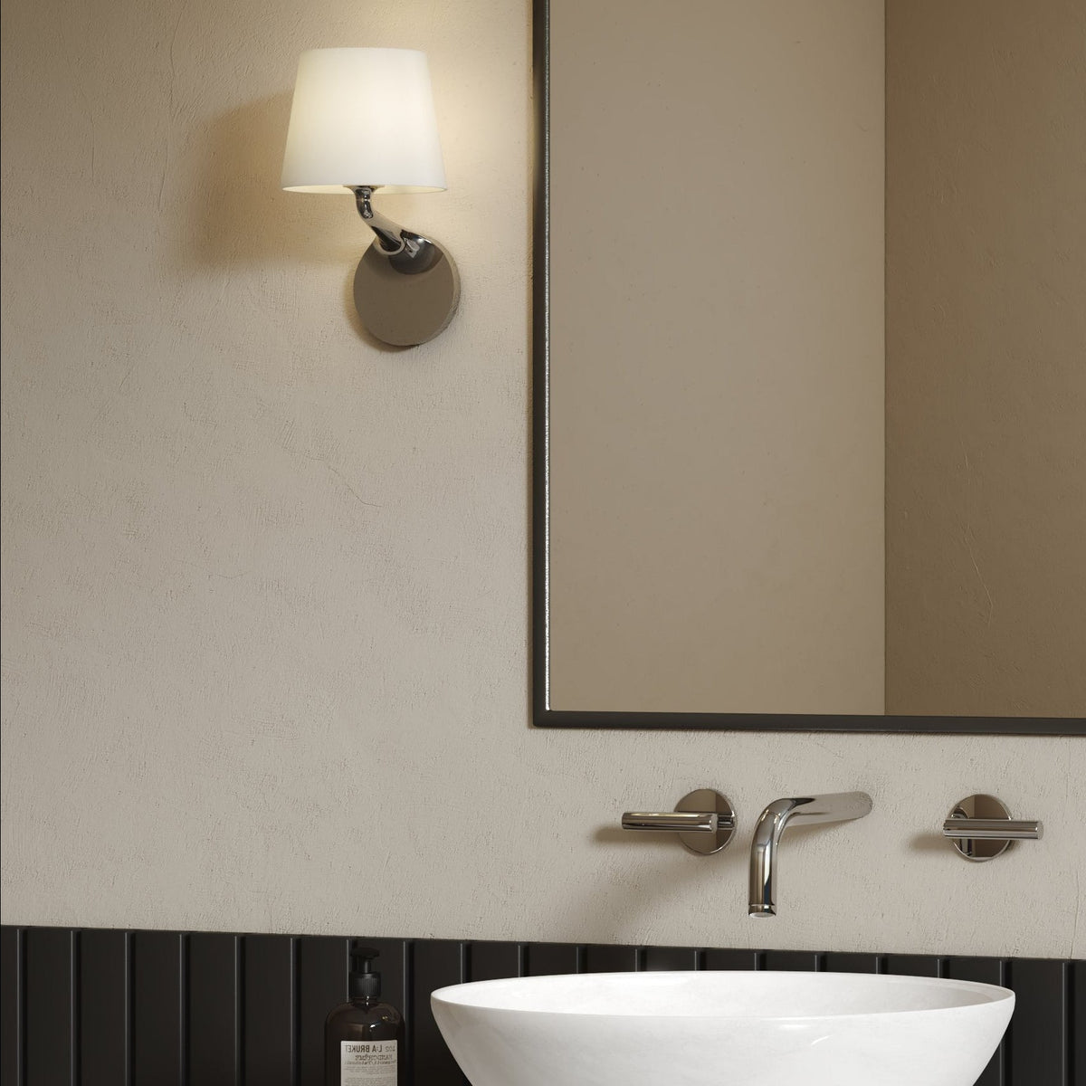 Wall-mounted light fixture with a white shade above a sink with a mirror and chrome faucet