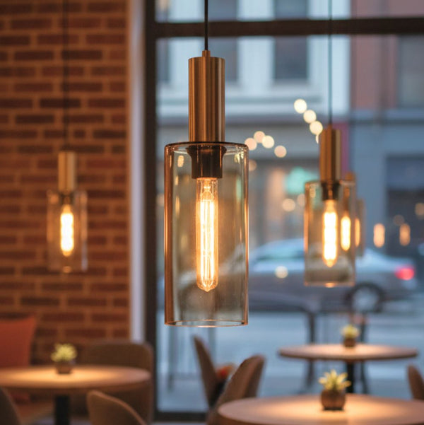 Three pendant lights with cylindrical glass shades and exposed filament bulbs illuminate a restaurant interior