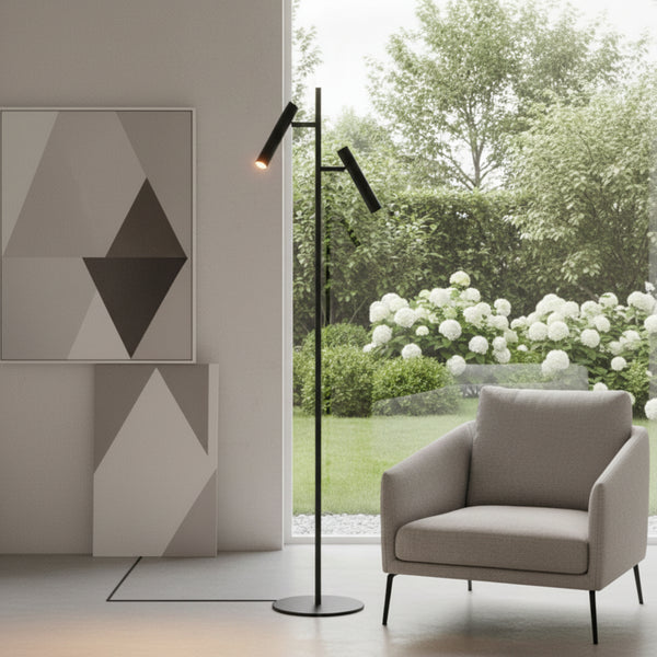 Black floor lamp with two adjustable lights next to a grey armchair and geometric art prints