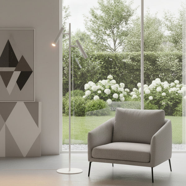 A modern living room with a grey armchair and a white floor lamp, overlooking a lush garden with white hydrangeas