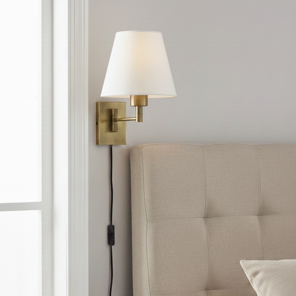 Brass wall sconce with a white fabric shade, mounted above a beige upholstered headboard