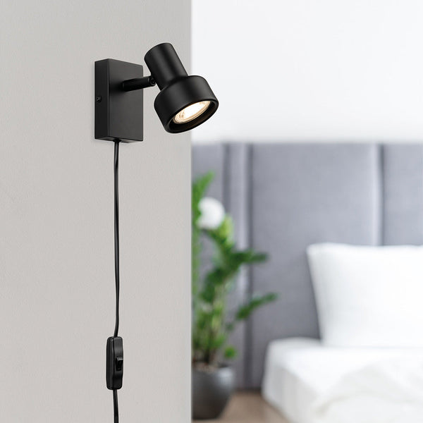 Black wall-mounted spotlight with a visible lightbulb and a power cord with an inline switch