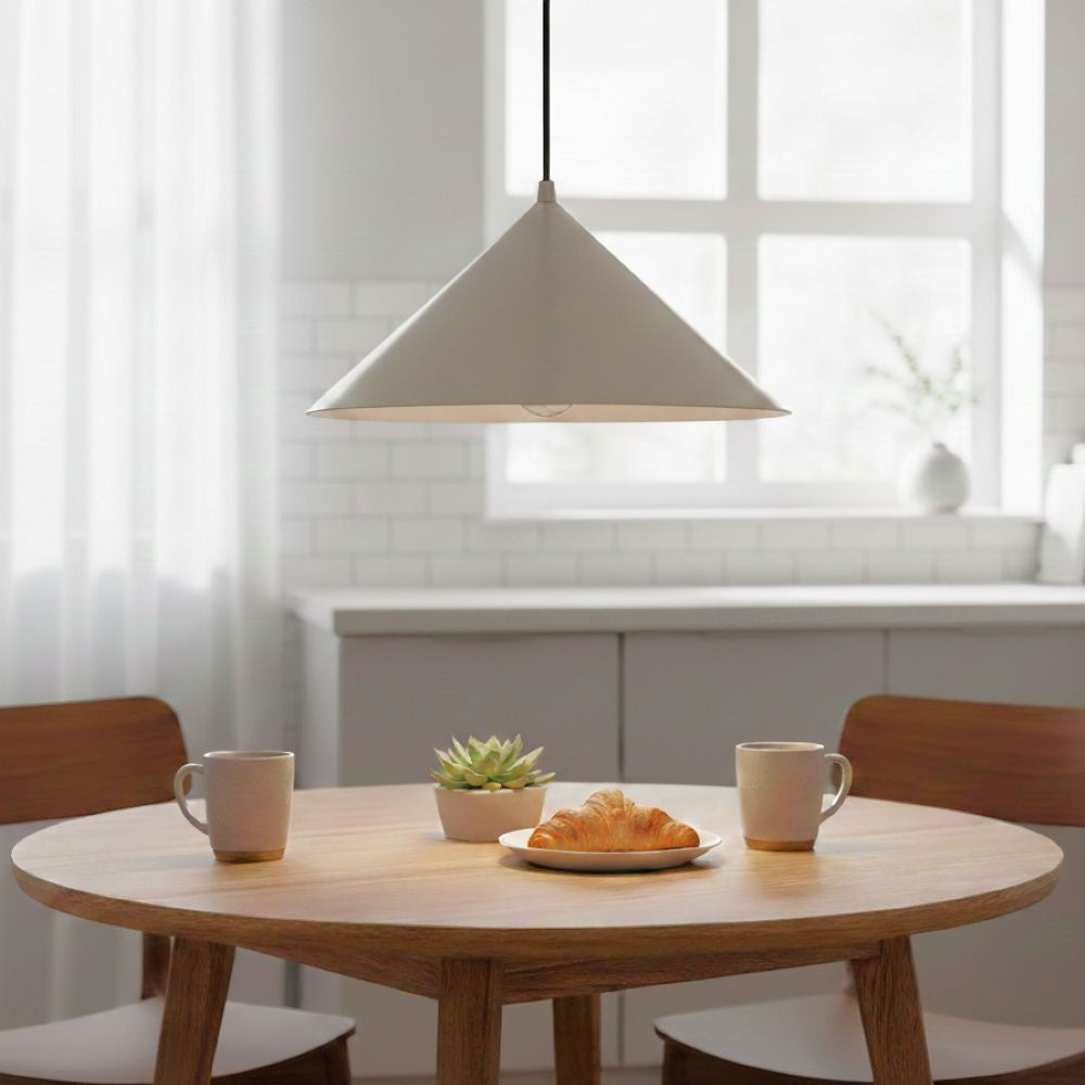 White conical pendant light hanging above a round wooden table with two mugs, a plant, and a croissant