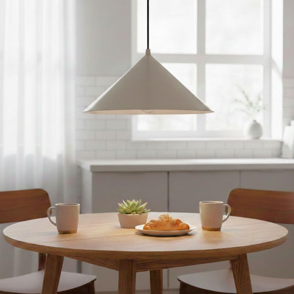 White conical pendant light hanging above a round wooden table with two mugs, a plant, and a croissant