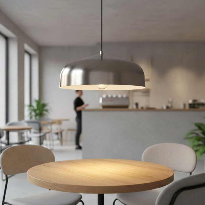 Silver pendant light hanging above a round wooden table in a cafe setting