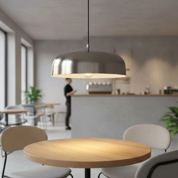 Silver pendant light hanging above a round wooden table in a cafe setting