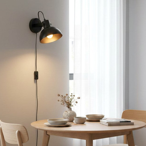 Black wall lamp with a gold interior shade illuminating a light wooden dining table