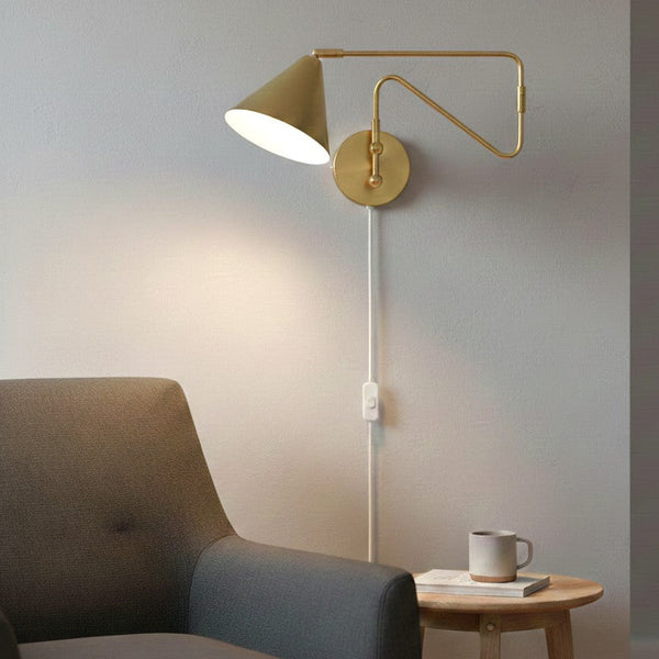 Brass wall lamp with a conical shade, illuminating a gray armchair and a small wooden side table with a mug