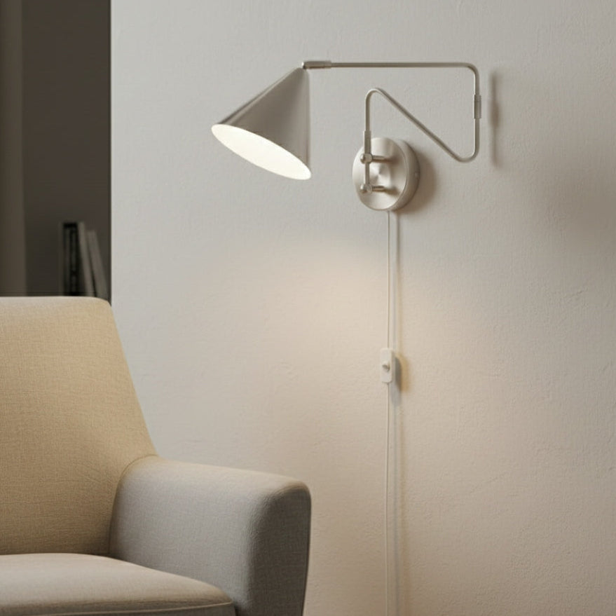 Brushed nickel wall sconce with a conical shade and adjustable arm, illuminating a light-colored armchair