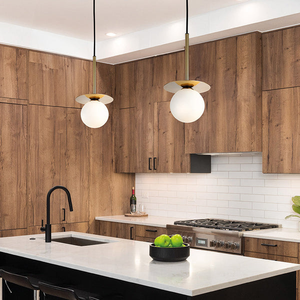 Two pendant lights with white globe shades and brass accents hang over a kitchen island