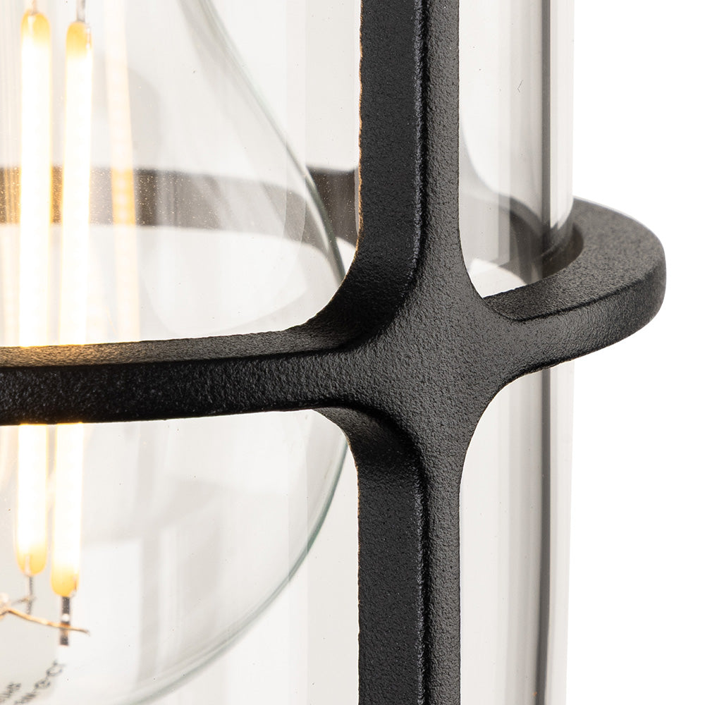 Close up of a black metal outdoor lantern with a clear glass shade and exposed filament bulb