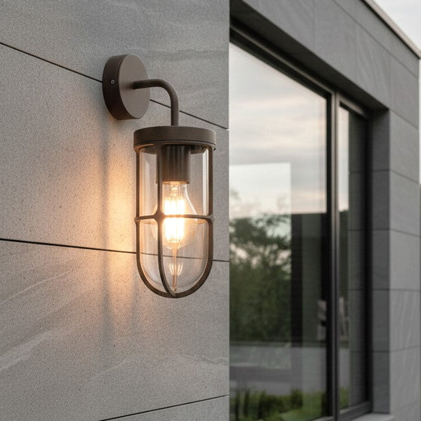 Outdoor wall light with a clear glass shade and a visible bulb, mounted on a grey tiled wall