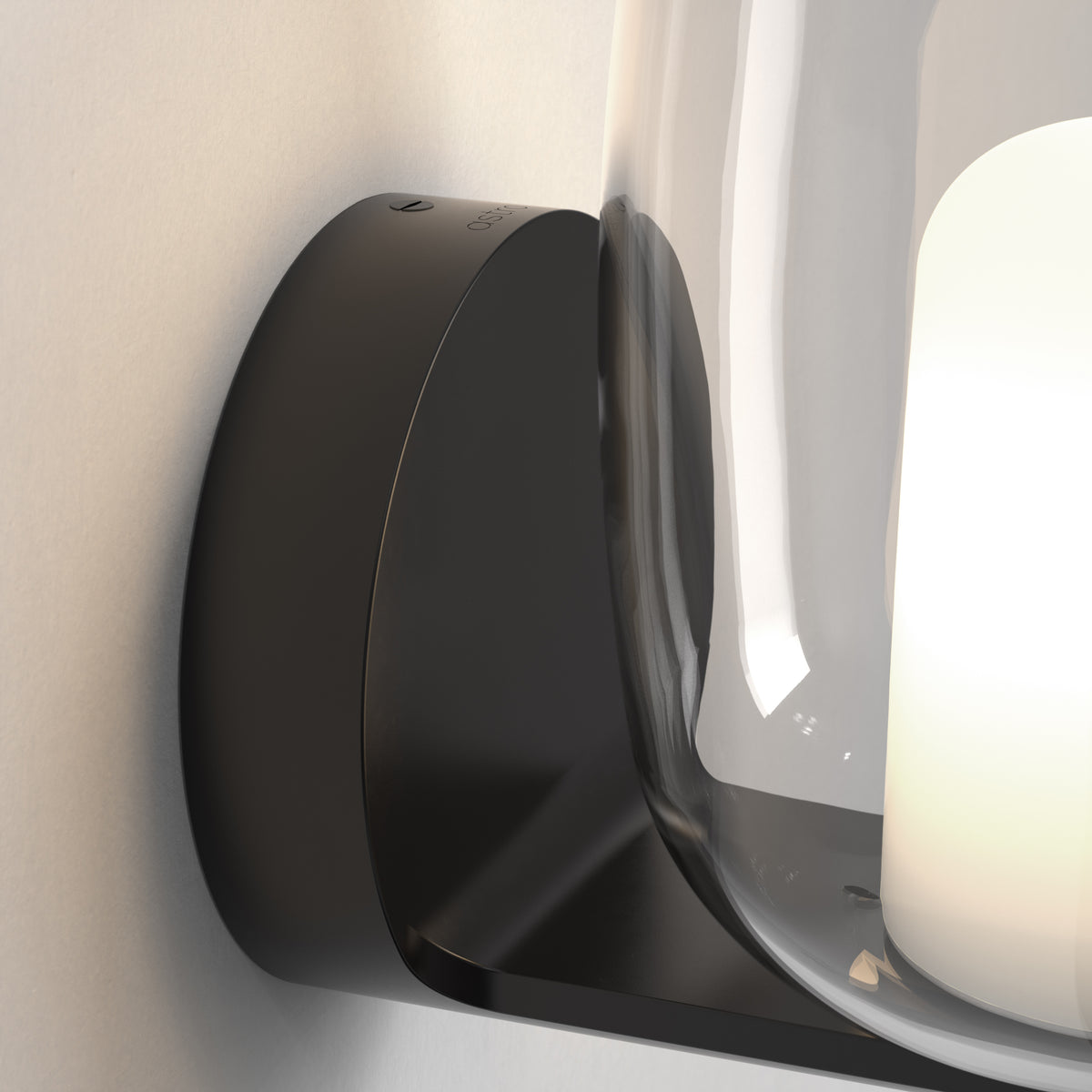 Close up of a black wall sconce with a clear glass shade and a white light source