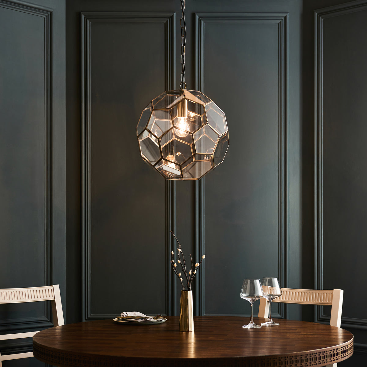 Geometric glass and brass pendant light hanging above a round dining table with two chairs.