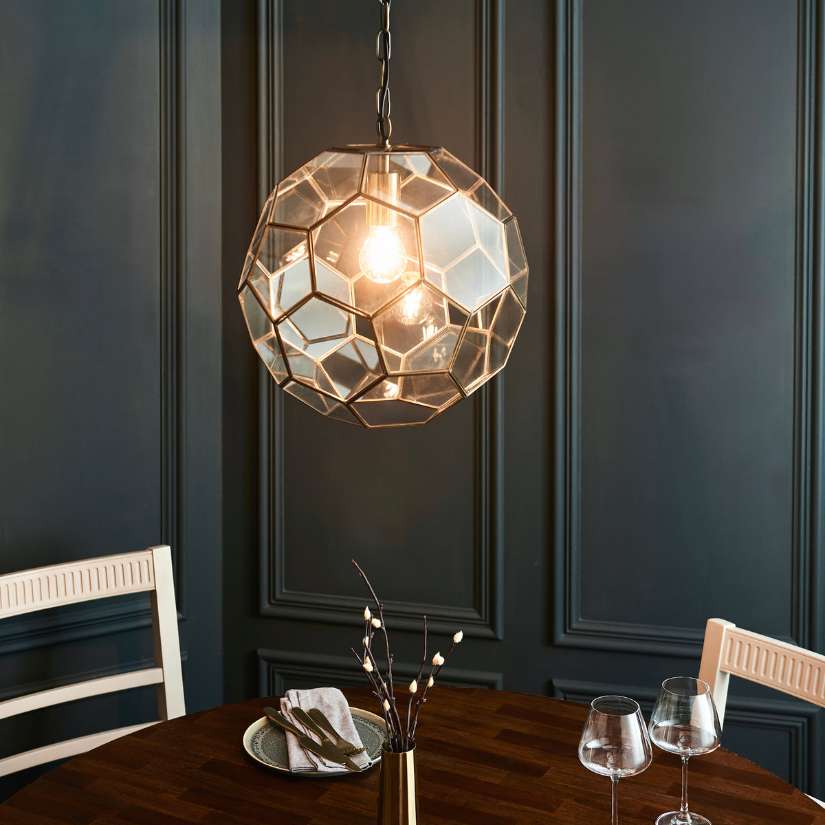Geometric glass and brass pendant light illuminating a dining table with two chairs.