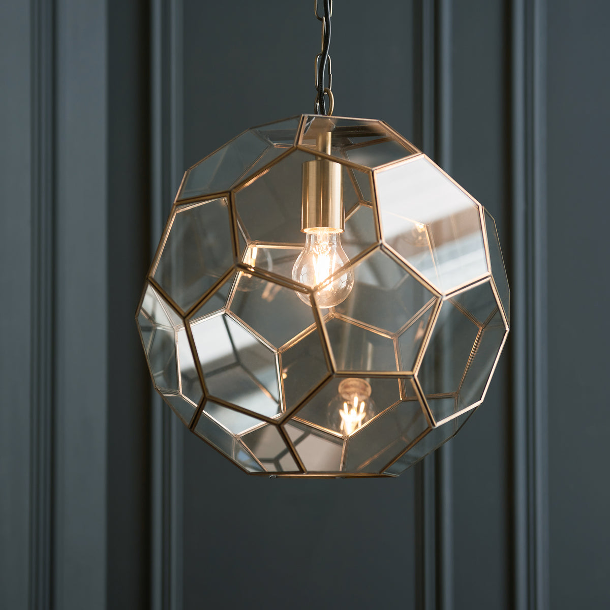 Close-up of a geometric glass and brass pendant light with an exposed bulb.