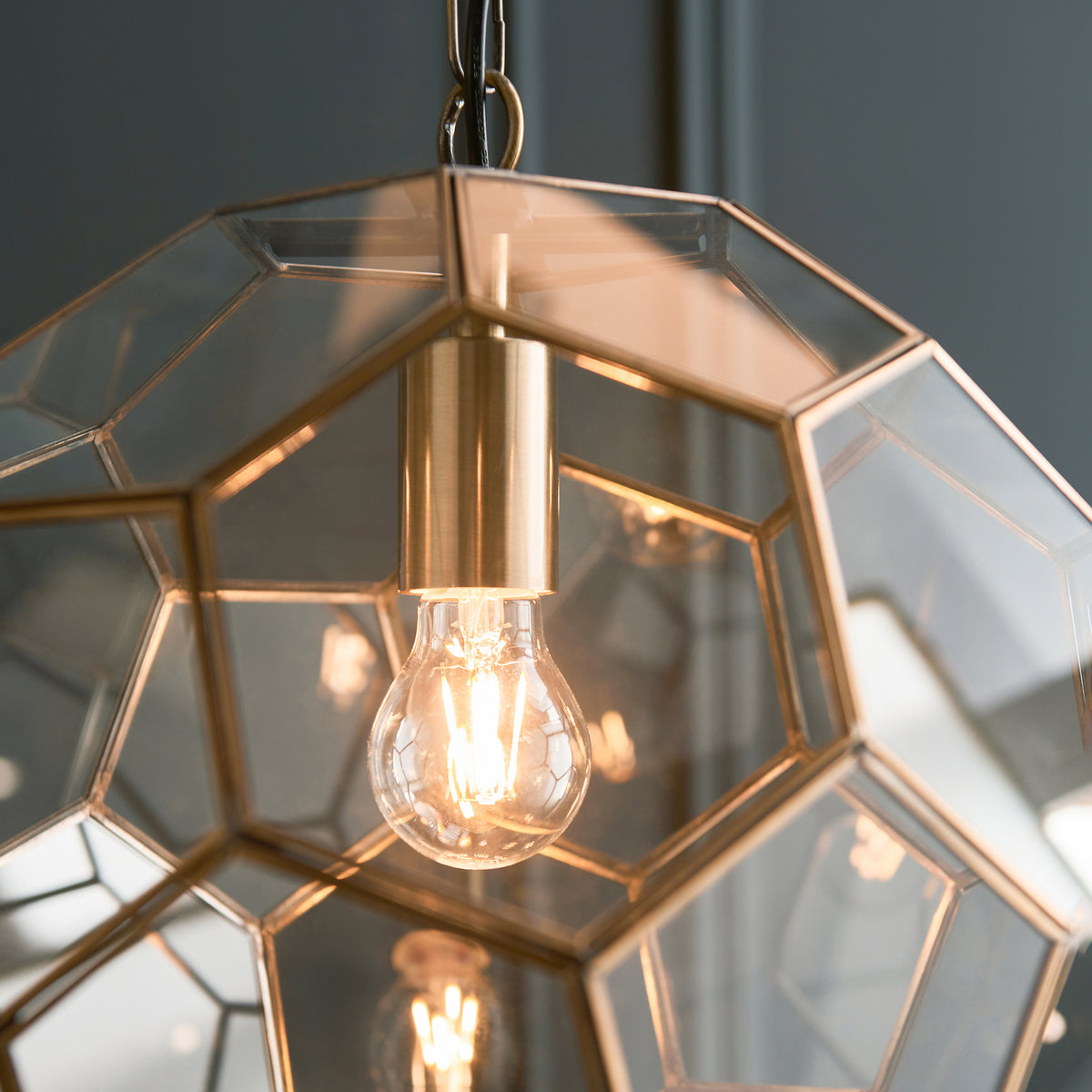 Close-up of the exposed bulb and brass fitting inside a geometric glass pendant light.