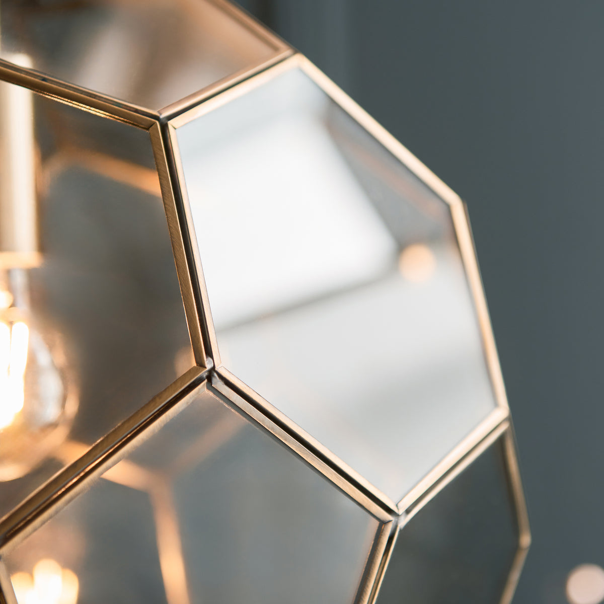 Close-up of the hexagonal glass panels and brass frame of a pendant light.