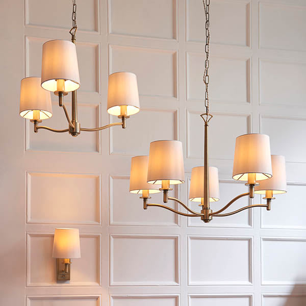 Two five-light chandeliers and a single wall light with cream shades against a white paneled wall.
