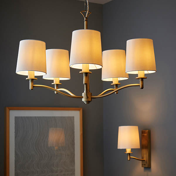 A five-light chandelier and a single wall light with cream shades illuminate a dark gray room.