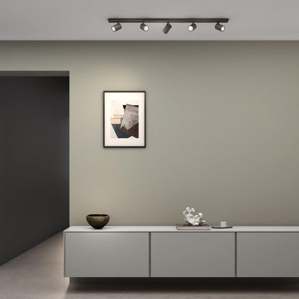 Four dark bronze track lights illuminate a framed abstract painting above a light grey console table