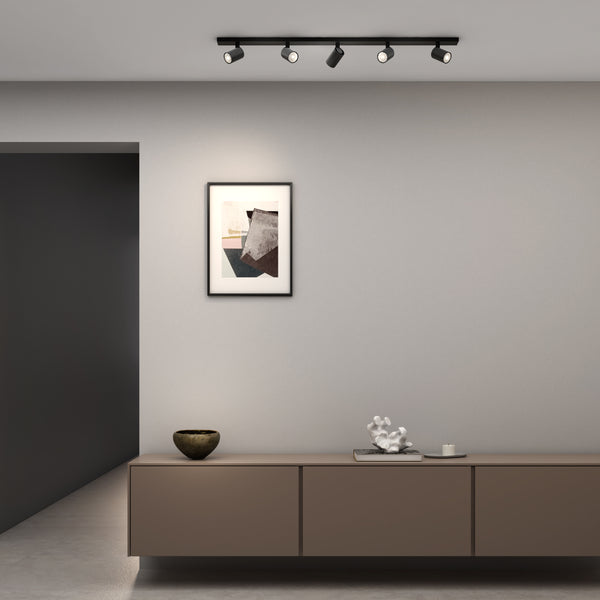 Black track lighting with four spotlights illuminating a modern living space with abstract art and minimalist decor