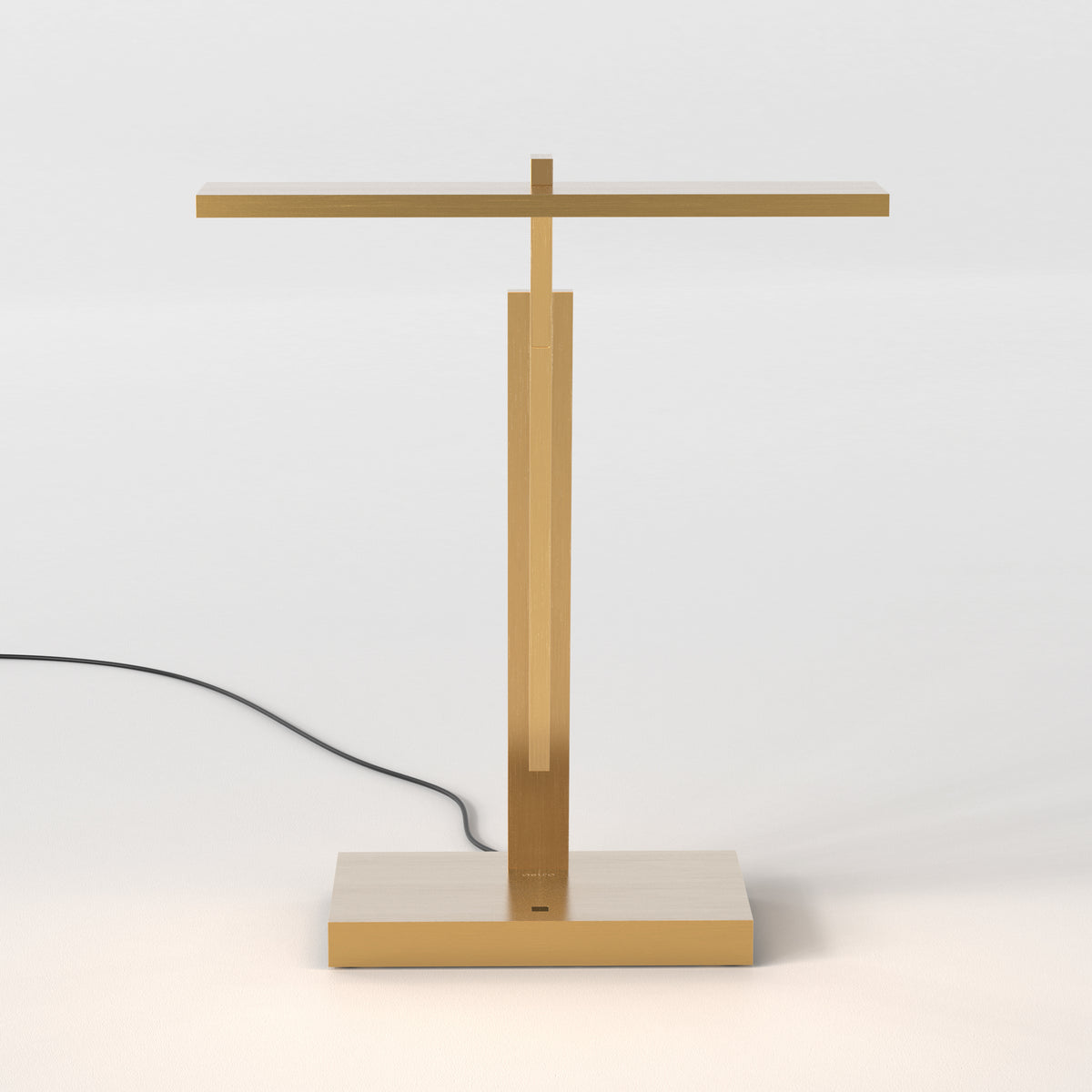 Gold metal table lamp with a rectangular base and a T-shaped top, emitting a soft glow