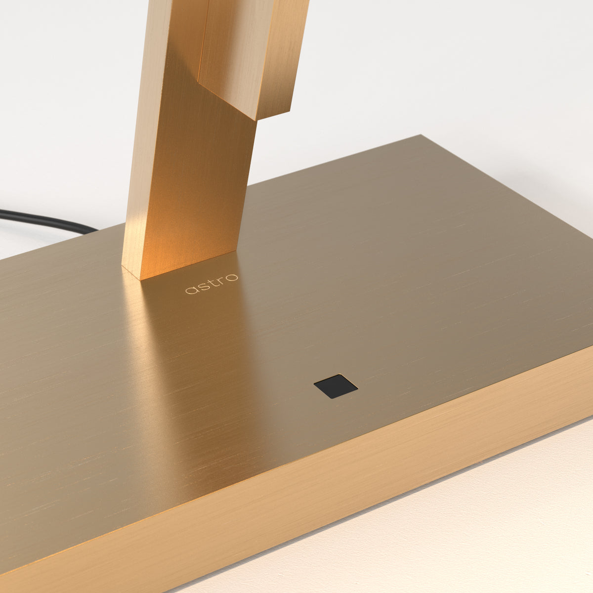 Close up of a gold lamp base with the word astro engraved and a small black square button