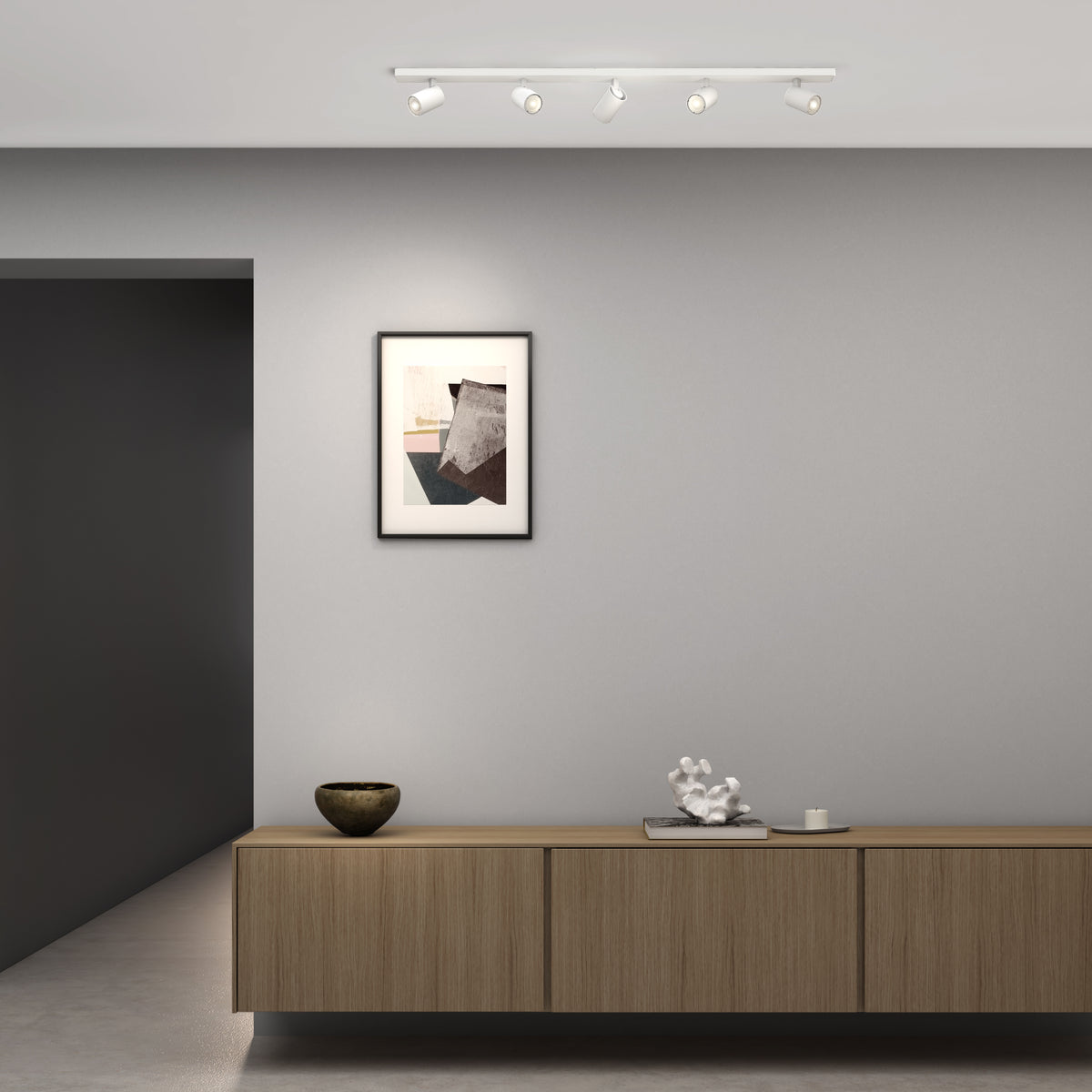 White track lighting with four adjustable spotlights on a ceiling above a framed abstract artwork