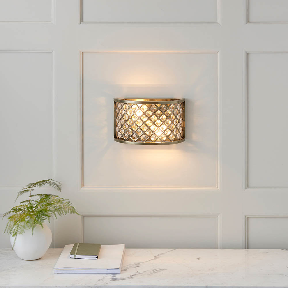 Antique brass wall light with crystal grid on a white paneled wall, casting light on a console table.