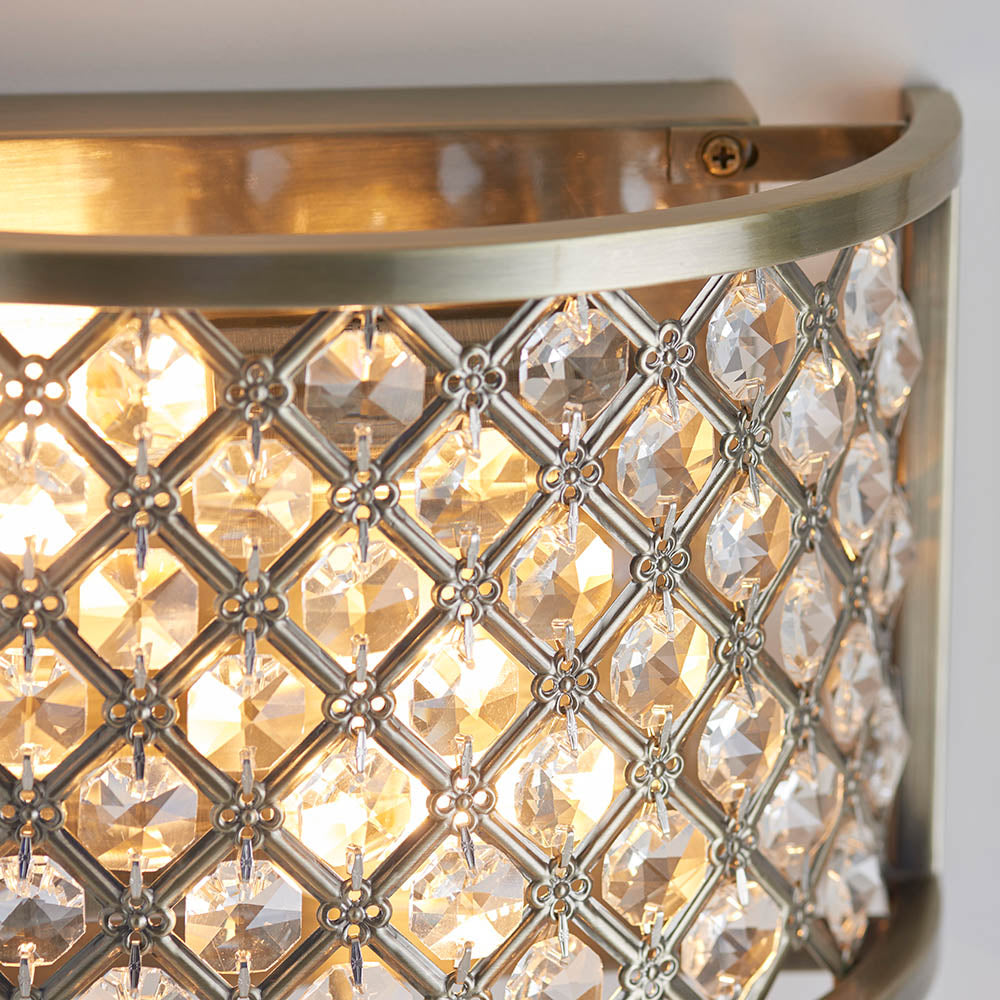 Angled close-up of a lit antique brass wall light, highlighting the crystal grid design.