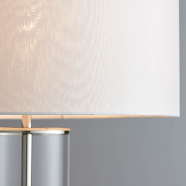 Close-up of the white fabric shade and clear glass column of a modern table lamp.